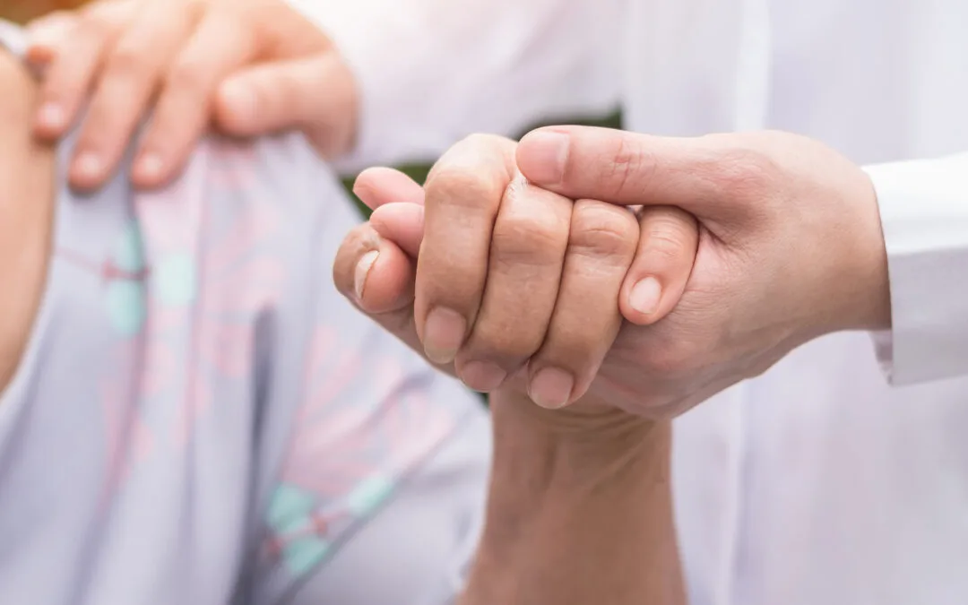 A clinician's hands gently holding a patient's hand in both of theirs